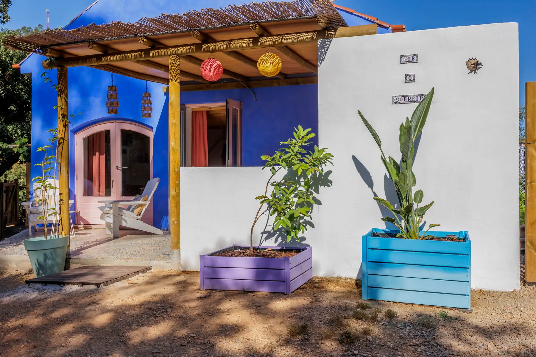The blue facade with its pergola, planters and a chair in the shade.